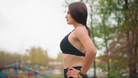Side view of athlete standing outdoors in game park with hands on waist, feeling relief, relaxed posture, fitness moment, healthy body, outdoor setting, emotional relief, peaceful expression
