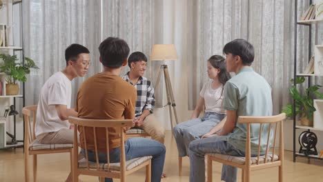 asian teen group sitting in chairs forming a circle discussing at home