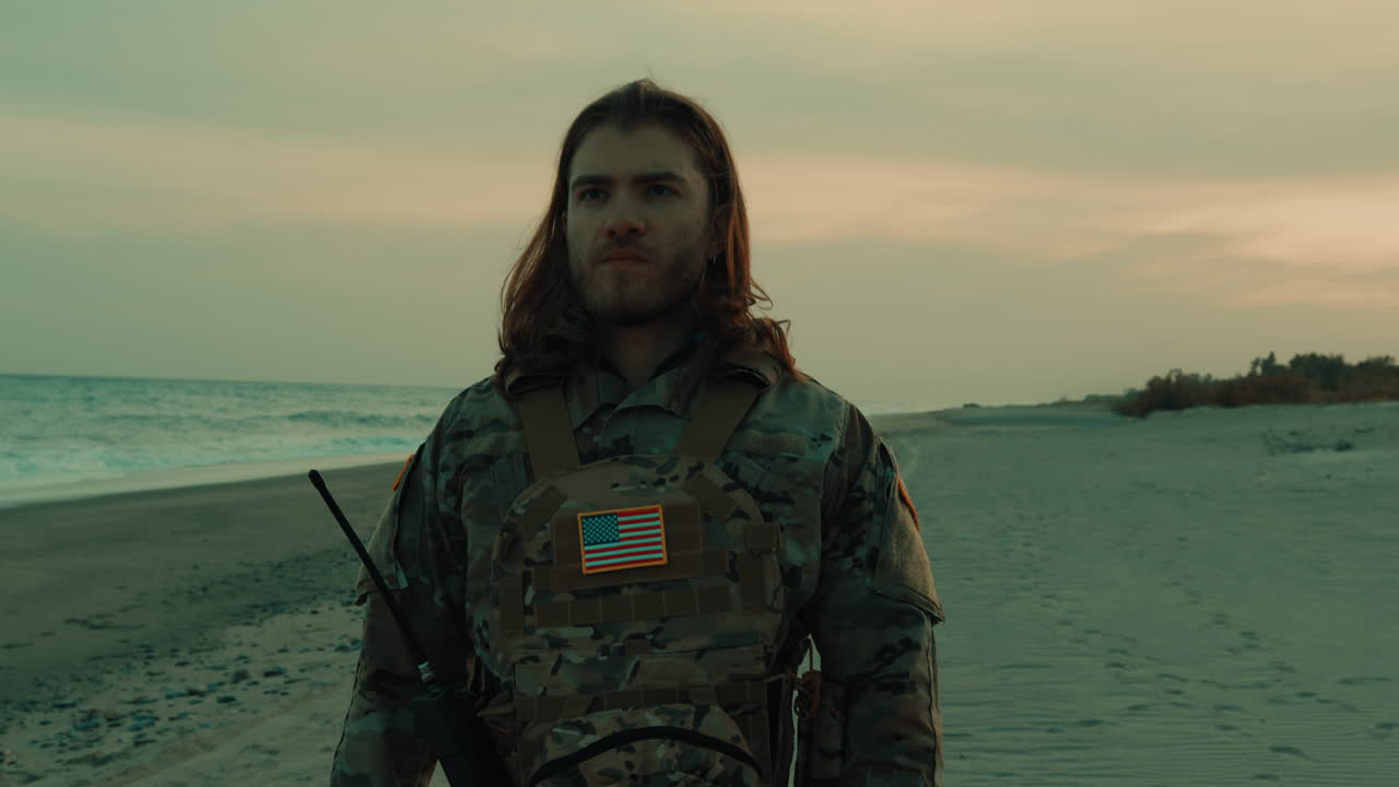 Jovem charmoso de cabelo comprido fazendo continência militar americana na praia