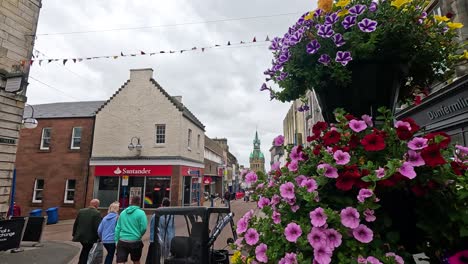 people walking past shops and flowers