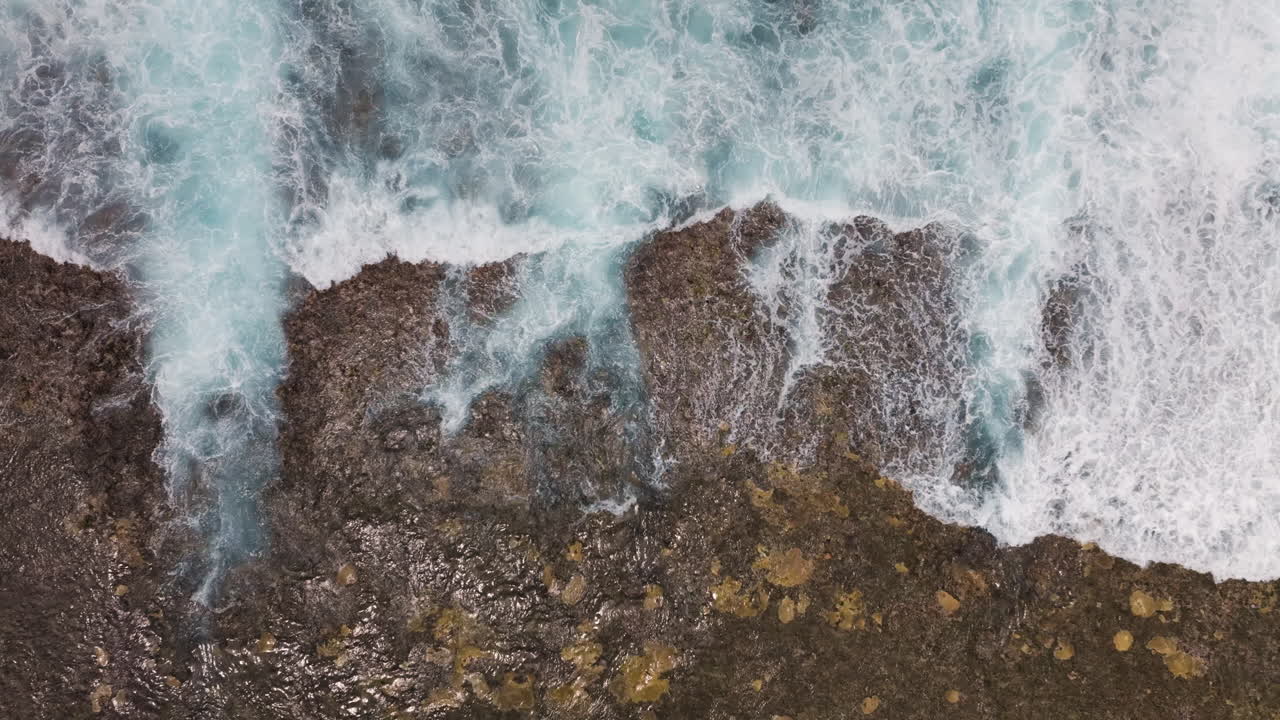 Aerial top down static of waves crashing over fringing reef in slow motion, dreamy soothing natural backdrop as tendrils drain