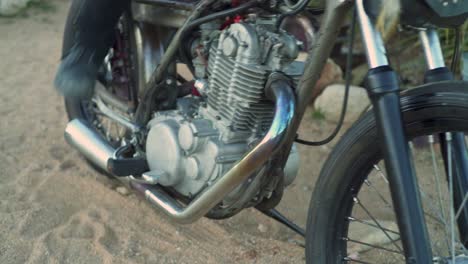 man in tall black boots tries to kick start vintage retro chopper motorcycle in the desert