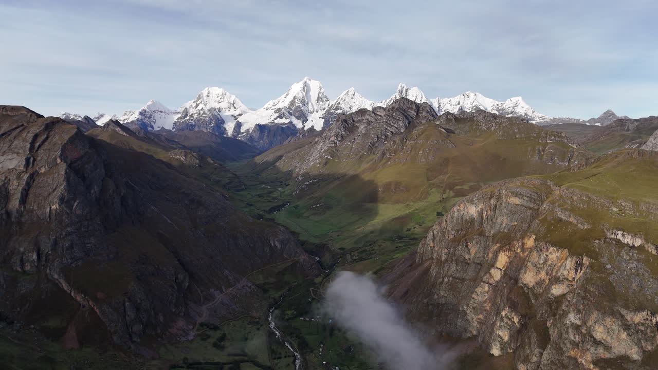 Cinematic aerial view of snowy Andes mountains in Peru with glaciers, rocky cliffs, and hidden blue alpine lake under misty clouds, dramatic landscape and natural travel destination