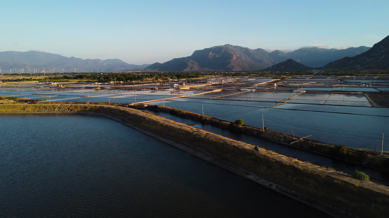 베트남의 소금 증발 연못 농장을 통과하는 좁은 오프로드의 공중 전망, 황금 시간 동안 자연 외딴 풍경에서 소금 수집을 위해 물 웅덩이 위로 드론 비행