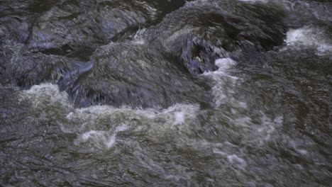 Nahaufnahme-Eines-Trüben-Flusses,-Der-über-Felsen-Im-Wasser-Fließt