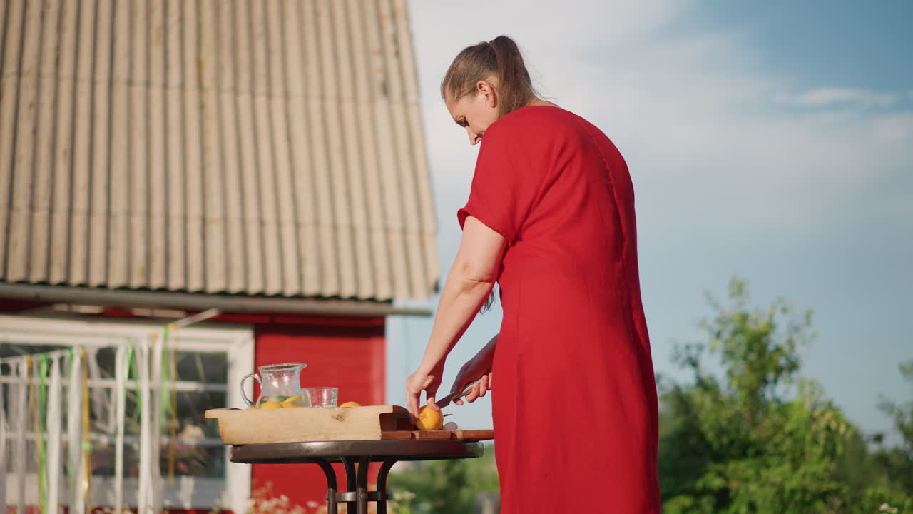 Kaukasische Frau in rotem Landhaus bereitet Produkte am Tisch zu, schneidet Gemüse auf Holzbrett. Sonnenlicht auf Dach und Gewächshaus. Praktische Morgenroutine, handzentrierte Komposition, ländliche Gelassenheit.
