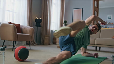 fit sportsman workout apartment. strong man making lifts legs arms in side plank