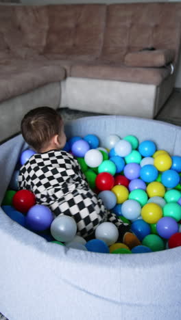 baby in checkered pajama tumbles in the dry pool. active playtime for a child at home. vertical video.