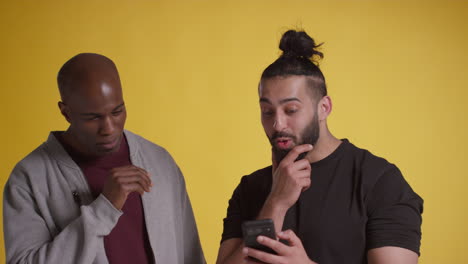 fotografía de estudio de dos amigos masculinos emocionados con teléfono móvil celebrando ganar dinero contra un fondo amarillo 4