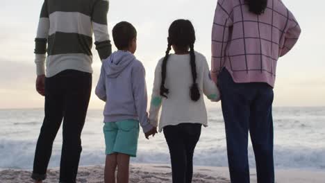 Back-view-of-hispanic-family-standing-on-beach-at-sunset