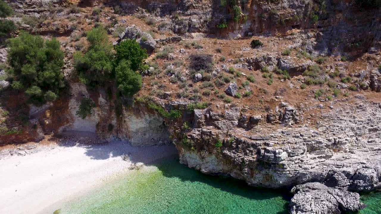 Tilting drone shot moving overhead revealing the white, sandy beachfront of a secret beach in Agriosiko, located in Cephalonia, Greece
