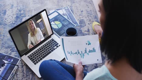 Mixed-race-businesswoman-sitting-on-floor-using-laptop-having-video-call-with-female-colleague