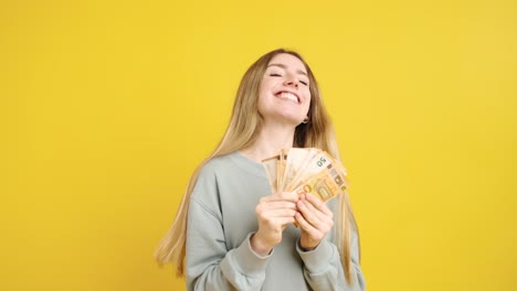 young woman holding and showing fifty euro bills on yellow background