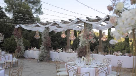elegant outdoor wedding dinner with luxurious decor. tables adorned with flowers and chandeliers, set under a pergola with lights. sophisticated and romantic atmosphere in a dreamy garden