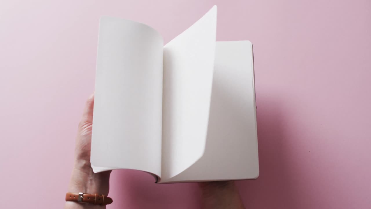 Close up of hand leafing through book with copy space on pink background in slow motion