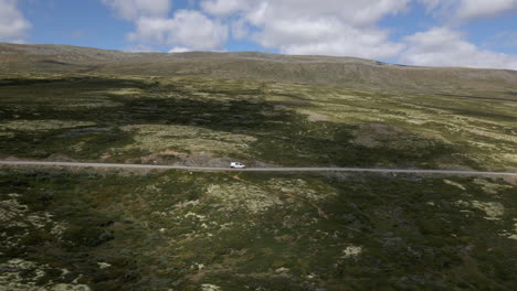 A-drone-shot-of-a-car-drives-along-a-mountain-road-with-cloudy-sky-background