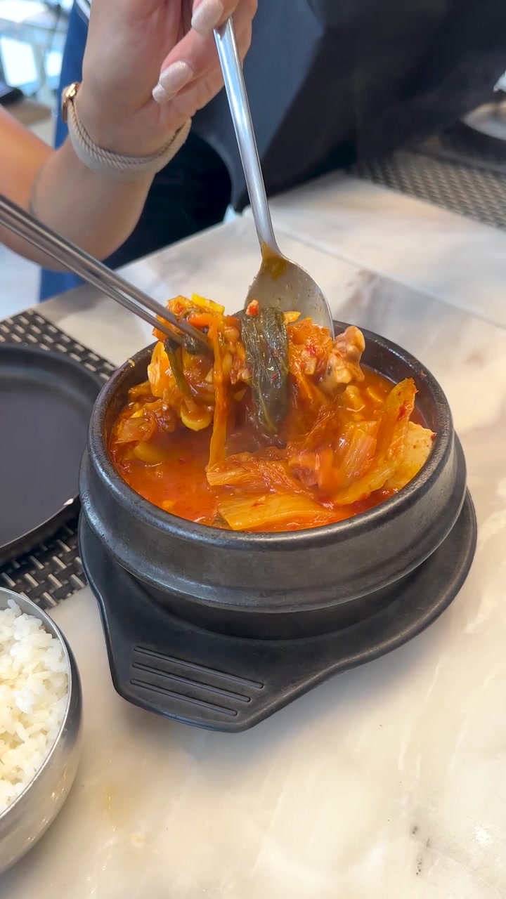 Seseorang menggunakan sendok dan sumpit untuk makan sup kimchi Korea pedas dari dolsot