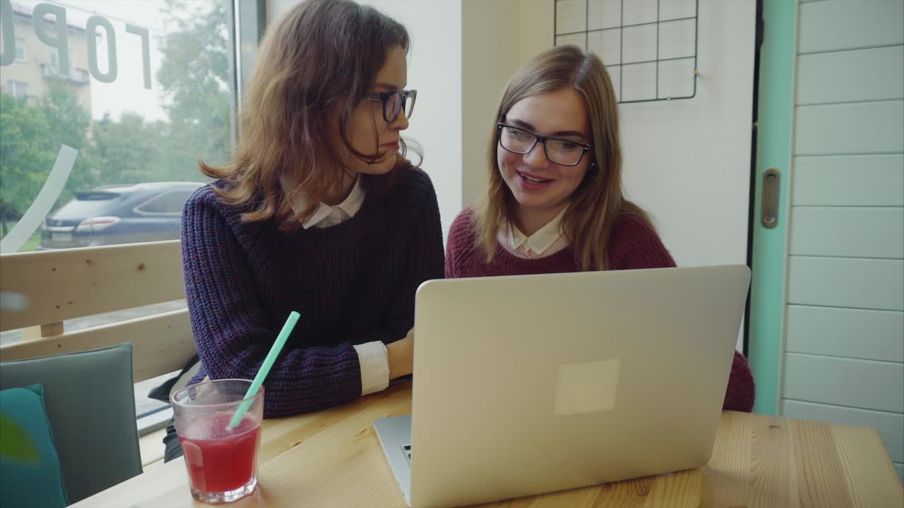 dos mujeres jóvenes trabajando en una computadora portátil en un café