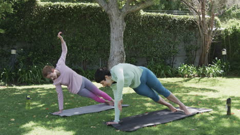 happy caucasian lesbian couple practising yoga in sunny garden, slow motion