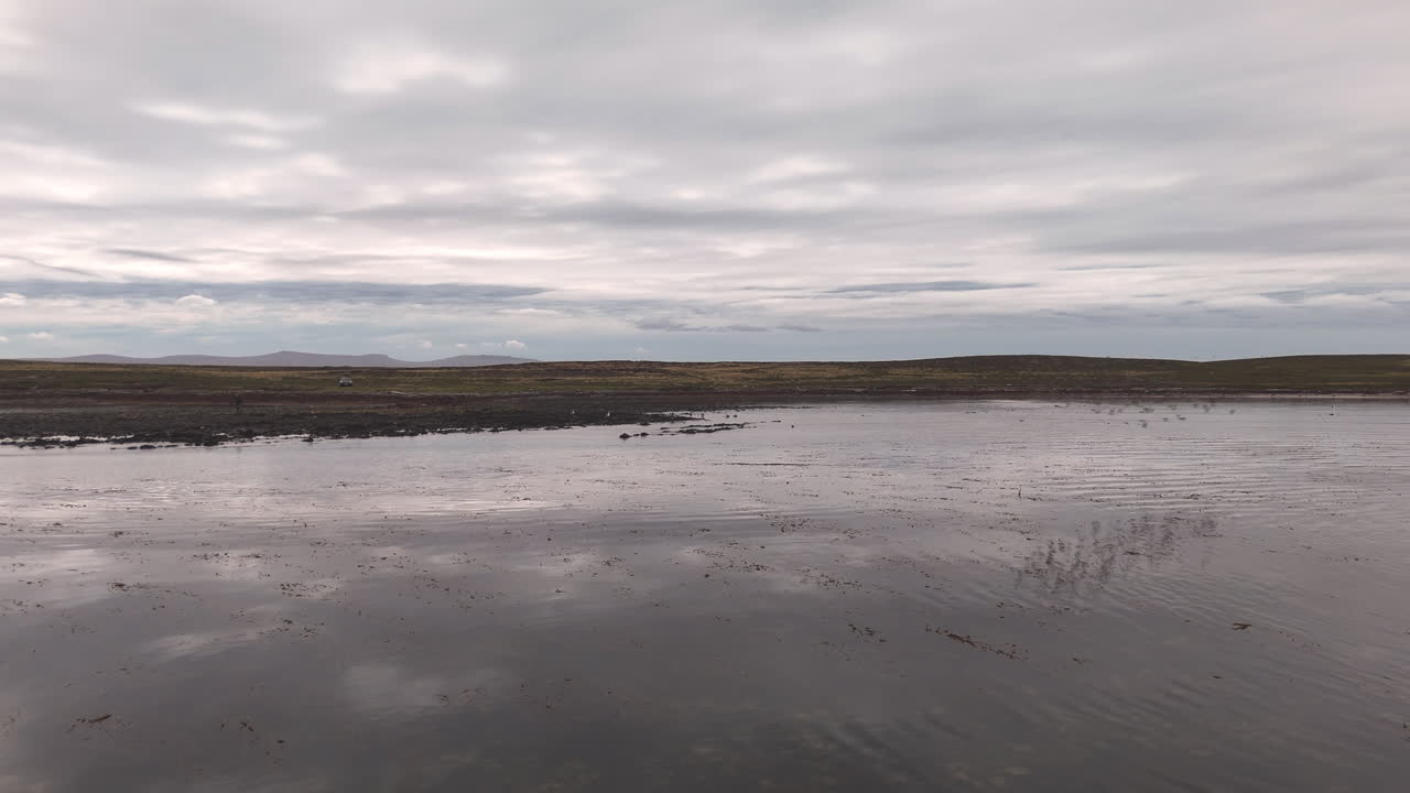 Aerial shot of water and landscape of East Falkland near Darwin Settlement in Falkland Islands (Islas Malvinas), South Atlantic. Birds flying through the frame