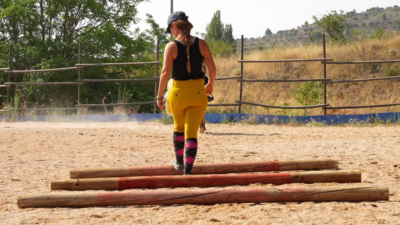 O instrutor organiza os obstáculos na arena enquanto os cavaleiros galopam, preparando o treino.