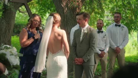bride and groom face each other at altar during officiant-led outdoor ceremony in slow motion, with happy smiling guests