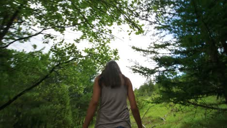 tiro bajo siguiendo detrás de los pies y las botas de una mujer que camina a través de densos bosques y árboles verdes en un día nublado