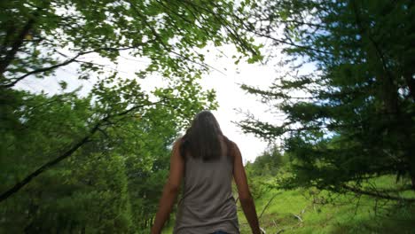 low shot following behind the feet and boots of a woman hiking through dense green woods and trees on a cloudy day