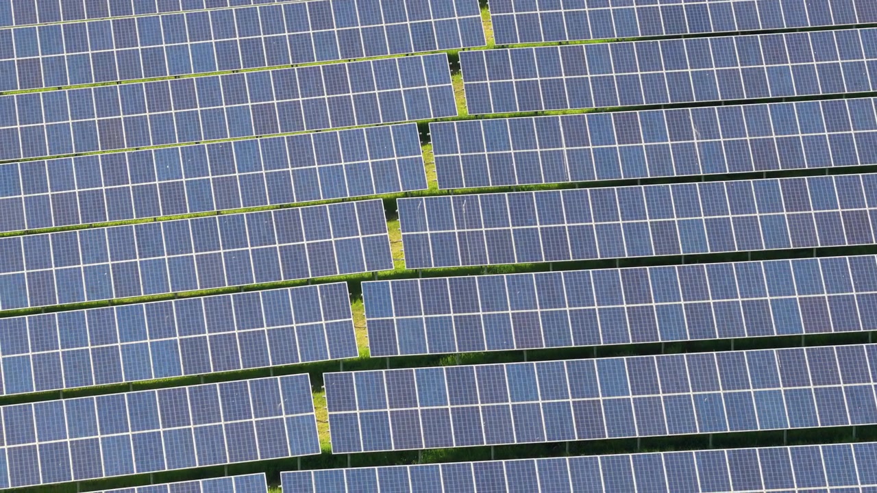 Veduta aerea dall'alto di file di pannelli solari fittamente raggruppate che riempiono l'inquadratura con celle fotovoltaiche blu e sottili strisce d'erba tra le schiere, Moravia, Repubblica Ceca.