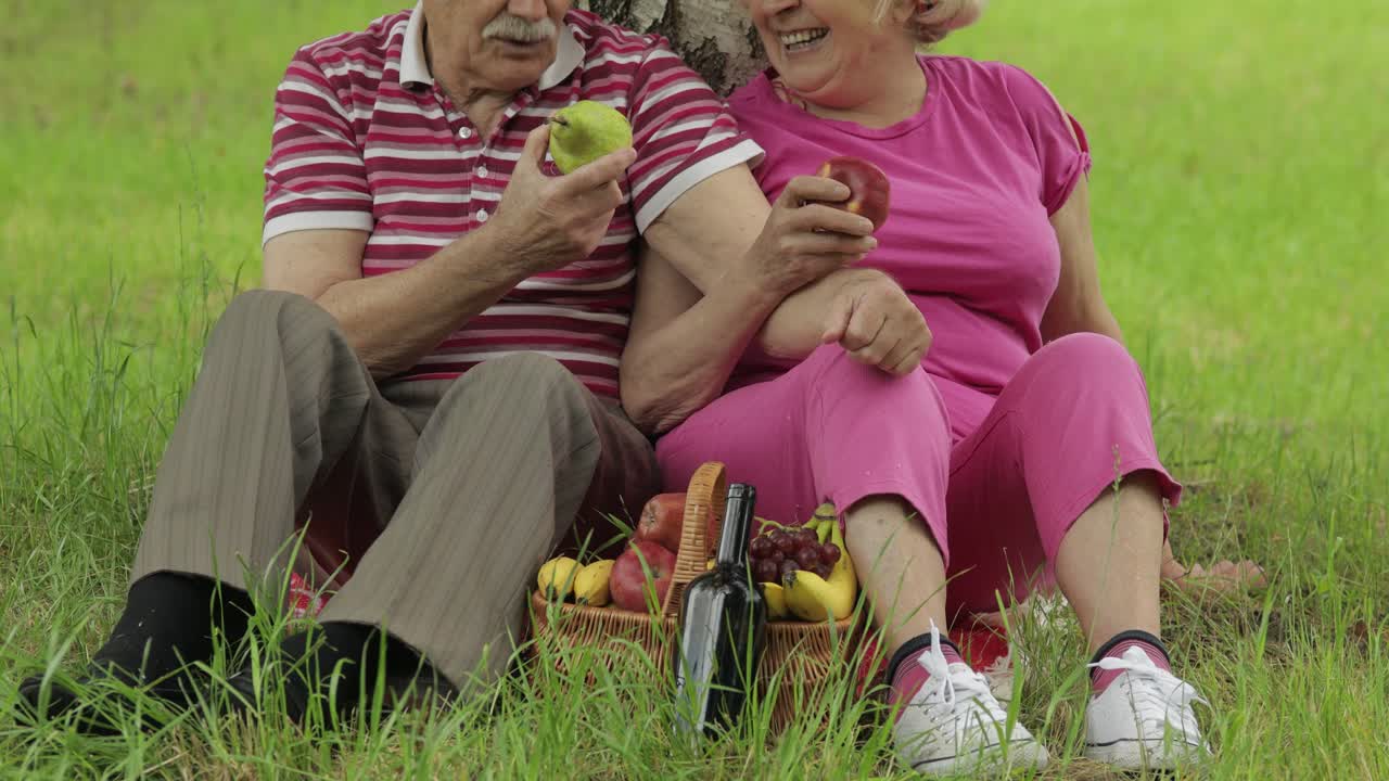 공원에서 주말 가족 피크닉. 활동적인 고령 백인 부부는 담요에 앉아 과일을 먹습니다.