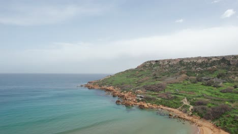 Drone-View-Over-An-Orange-Rocky-Shoreline-With-Turquoise-Water,-Gozo-Island,-Malta