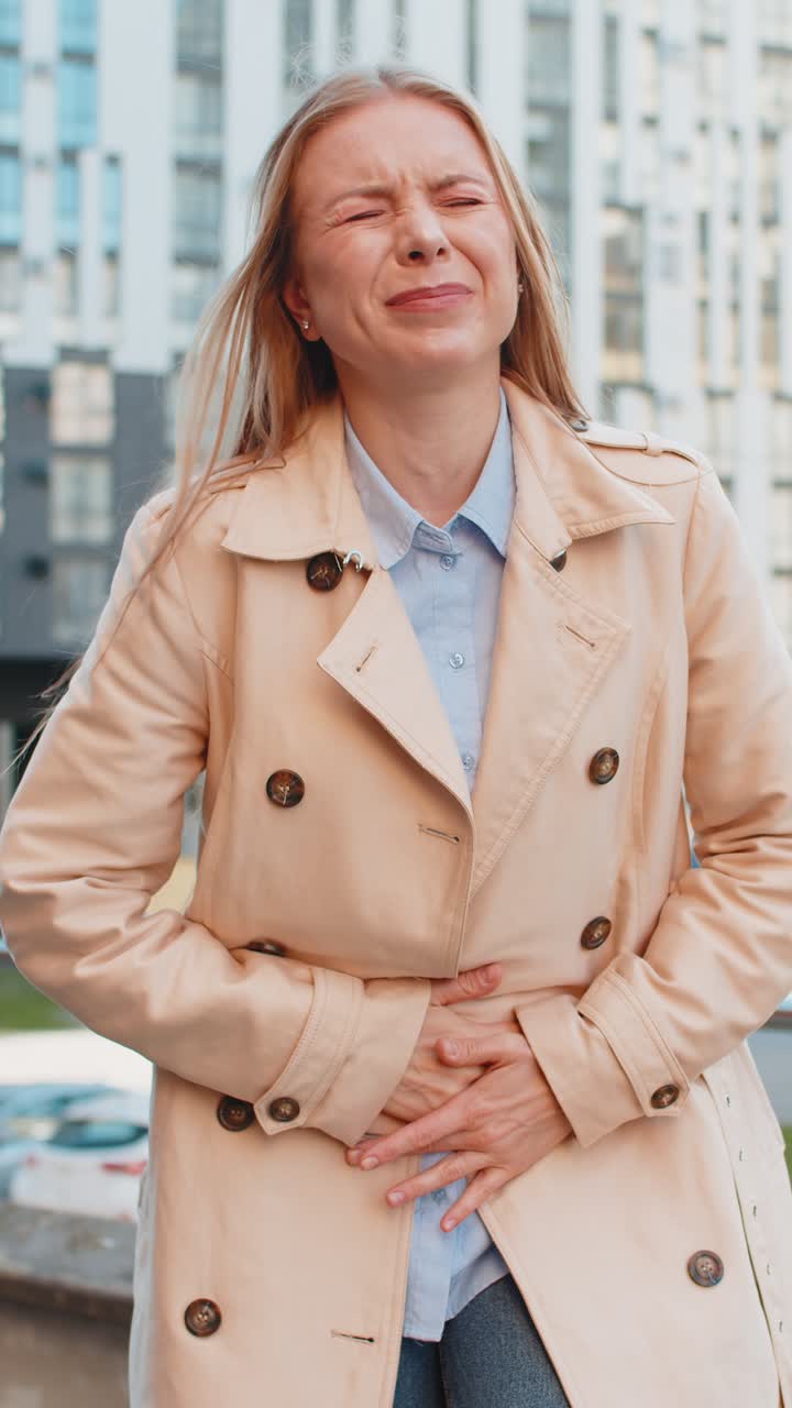 Caucasian mature businesswoman feeling sudden strong abdominal stomach pain problem on city street
