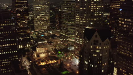 In-between-Skyscraper-Canyon-of-a-big-City,-Los-Angeles-California-at-Night-with-lit-up-illuminated-Skyline-Towers,-Aerial-Wide-Angle-Shot