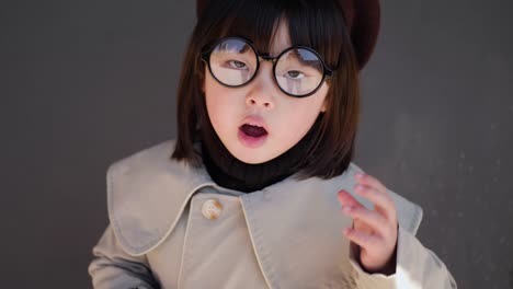 회색 코트와 모자를 입은 한국 소녀는 가게의 유리 문에서 봄에 거리에 서 있습니다.