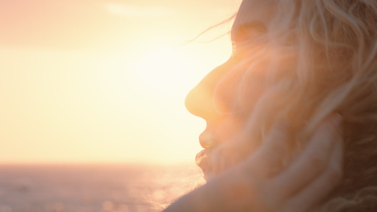 ritratto ravvicinato di una bellissima donna bionda che si gode il mare tranquillo al tramonto contemplando il viaggio esplorando la spiritualità sentendo la libertà con i capelli soffiati dal vento