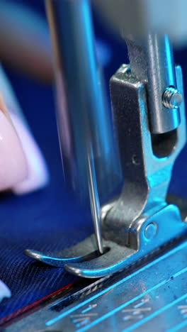 female hand pushes material through a sewing machine. sewing machine needle rapidly moves up and down. tailor sews blue fabric in the sewing workshop. close-up. vertical video