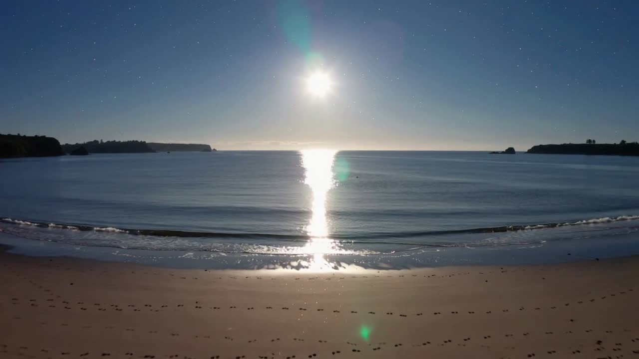Panning camera revealing wet sand with footprints and pebbles at cove, following sun path