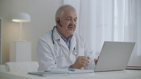 cheerful male doctor is communicating online with colleagues or patients by laptop using video call