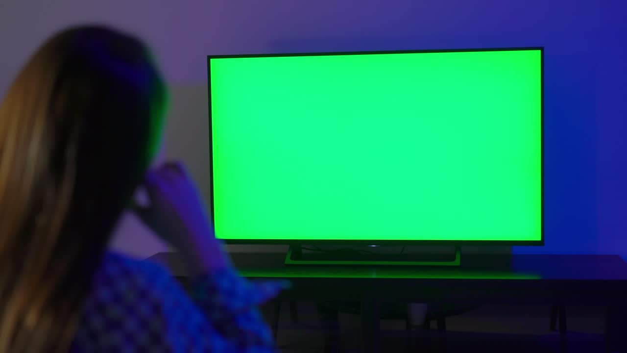 una mujer joven se sienta en un sillón y mira la televisión.