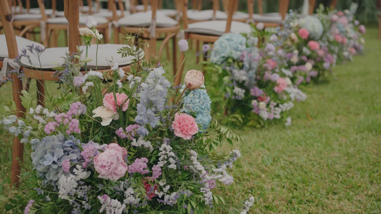 Sedie per la navata nuziale adornate con fiori color pastello disposti sull'erba