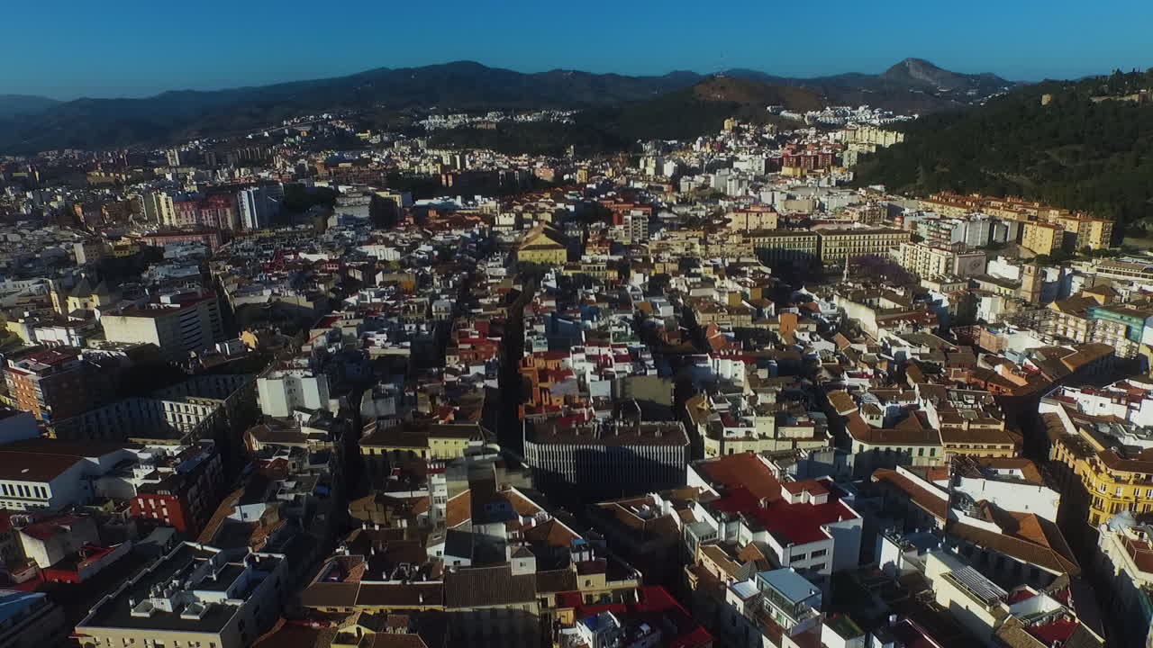Il drone avanza in diagonale su Malaga, poi si inclina verso il basso in una vista dall'alto dei tetti illuminati dal sole