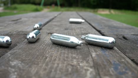 Multiple-chrome-drug-nitrous-oxide-laughing-gas-drug-cylinders-pan-left-across-wooden-park-bench