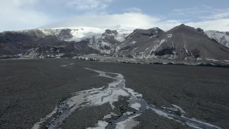 aerial video flying low along a skeidararsandur black sand deposit at the foot of snow-capped mountains