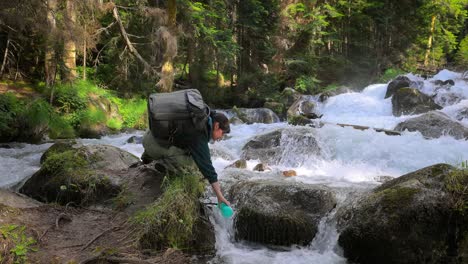 Reisende-Frau-Mit-Rucksack,-Trinkwasser-In-Der-Natur-Im-Wald-In-Der-Nähe-Eines-Gebirgsflusses.