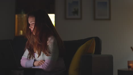 anxious woman sitting on sofa at home at night looking at laptop concerned about social media or bad news 10