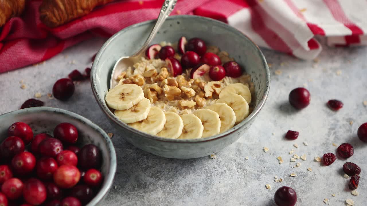 Ciotola in ceramica di porridge d'avena con banana, mirtilli rossi freschi e noci.
