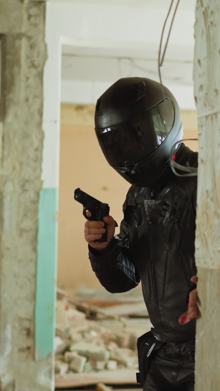 Fighter in black helmet with handgun looks from behind broken brick wall hiding from bad guys in old abandoned building corridor slow motion