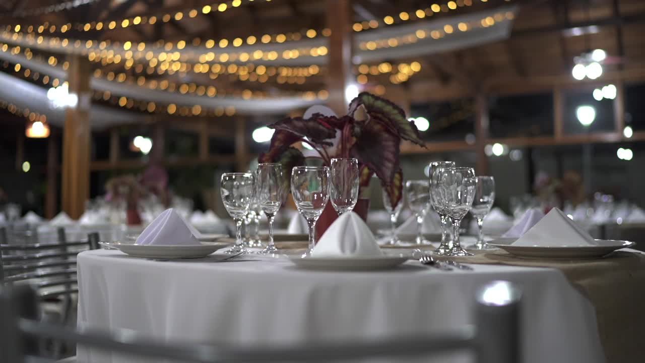 Parallax-billede af elegant bryllupsbord med hvide bordopdækninger, potteplante med begonie og bokeh-lys i baggrunden