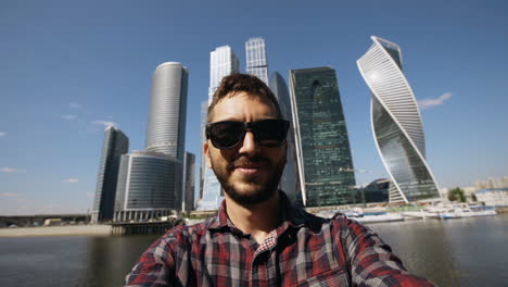 man takes selfie in front of skyscrapers