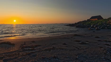 Midnight Sun Time Lapse. With seaweeds scattered on sandy shore and abandoned red cabin with black roof. Lofoten islands, Northern Norway